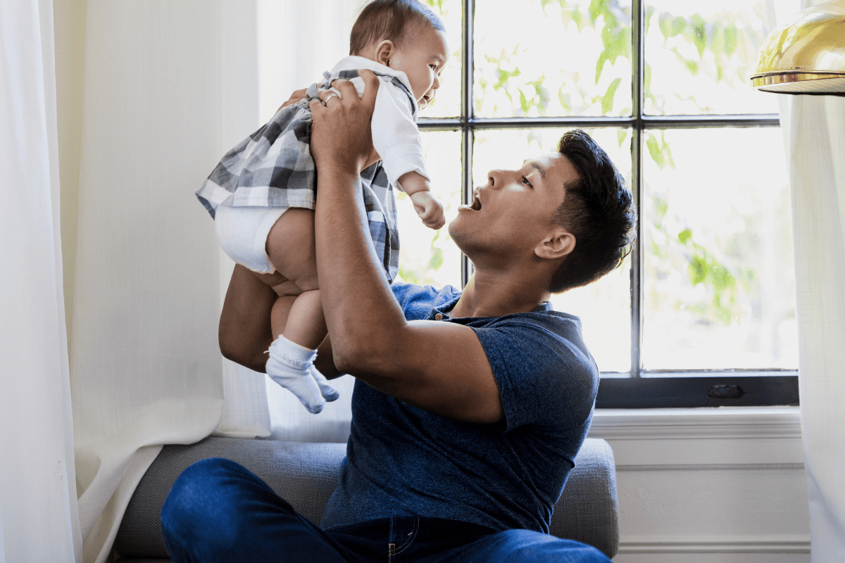 dad lifts baby by sunlit window