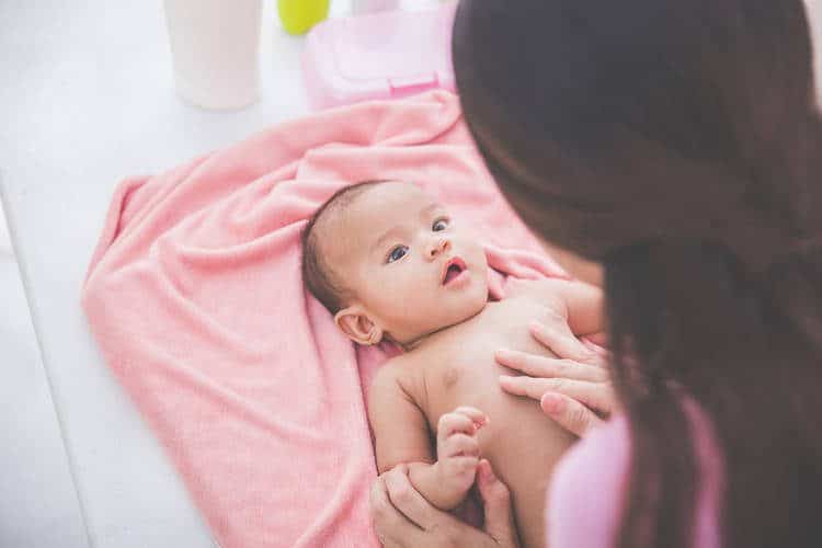 A baby lays on back on a pink blanket and caretaker tends to it. 