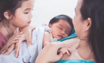 Baby Sleeping in mother's arms with sister watching