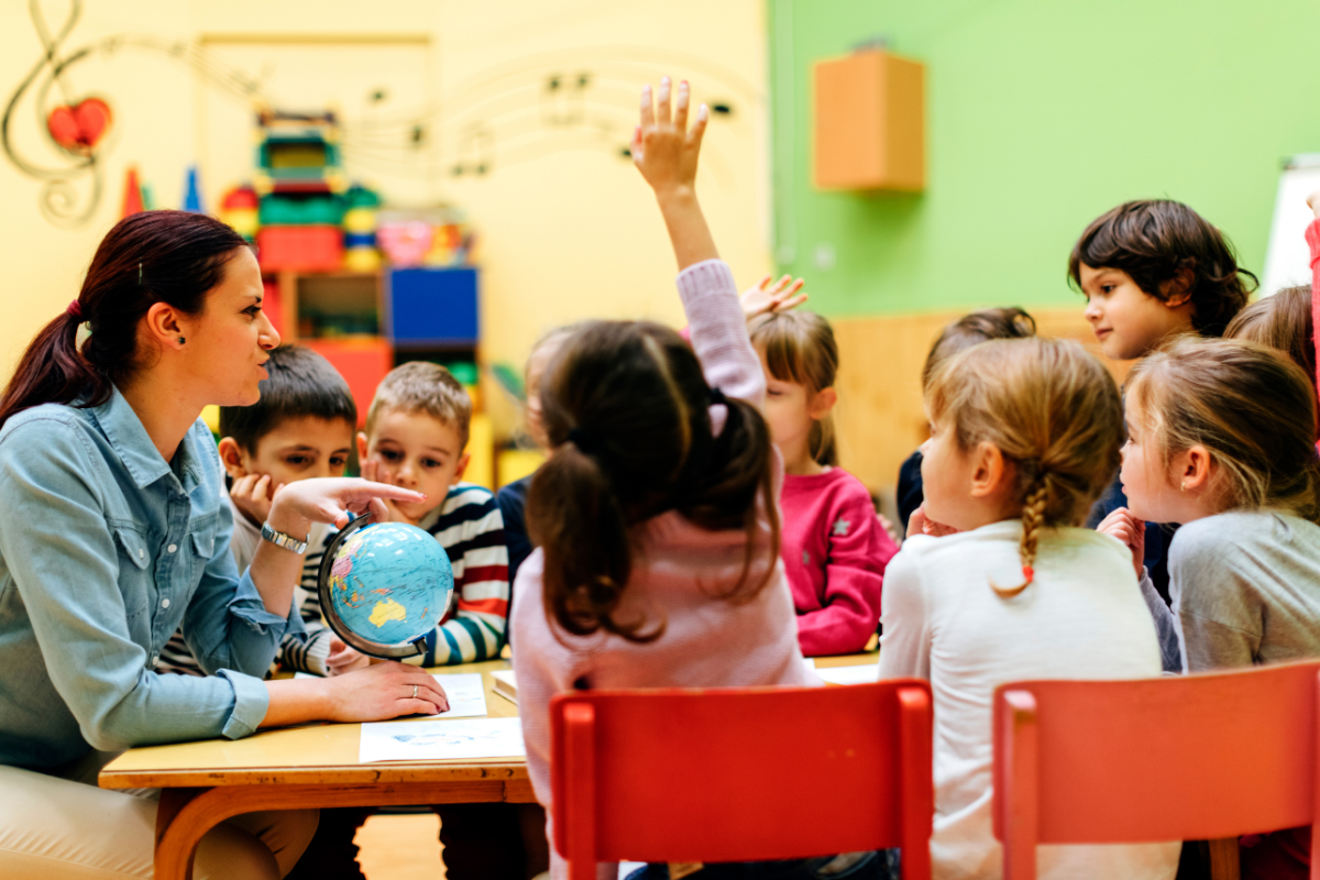 child in red chair raises hand in preschool classroom