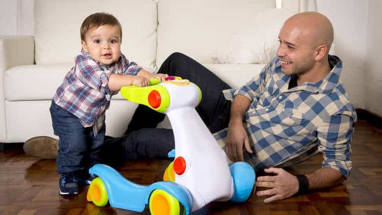 dad smiles at baby boy pushing toy