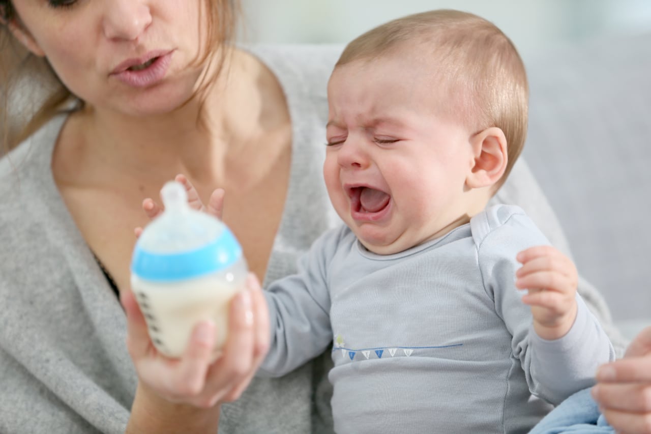 a mother holds a crying baby and a bottle in her hand