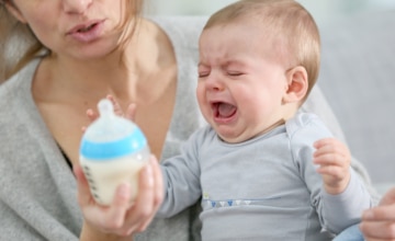 a mother holds a crying baby and a bottle in her hand