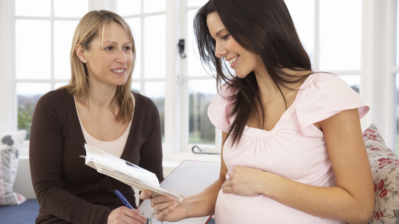 pregnant woman reading book and talking to other woman