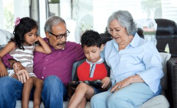 grandparents sit on couch with grandchildren on ipad
