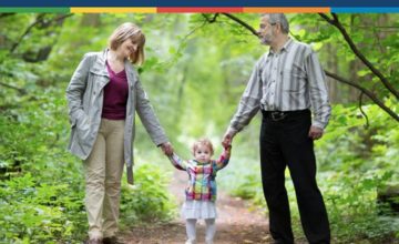 Toddler standing and holding the hand of a man and a woman