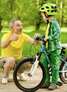 Man squatting and child with bicycle and bicycle helmet looking at him