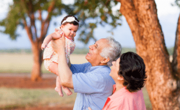 grandparents hold baby in air at park