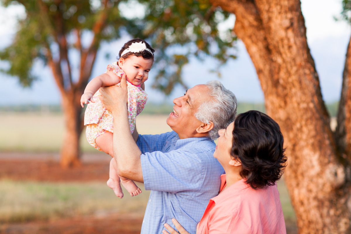 grandparents hold baby in air at park