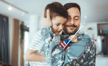 military dad embraces son holding flag