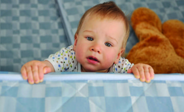 A baby peeks over a crib wall.