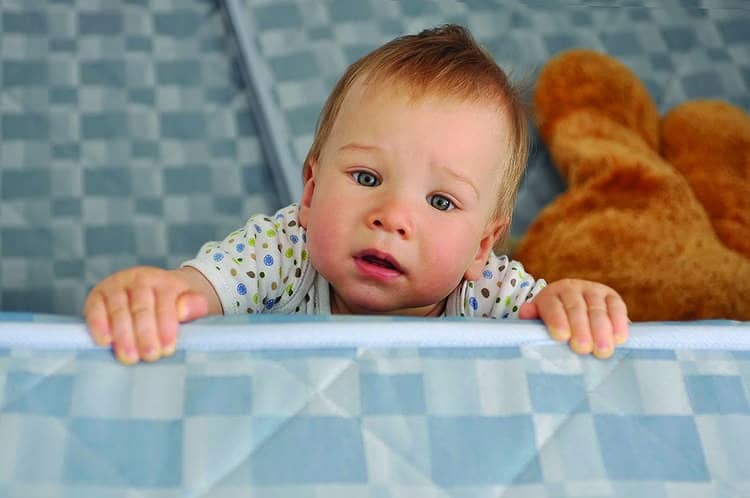 A baby peeks over a crib wall.