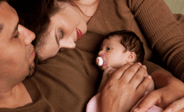 parents wearing brown hold newborn