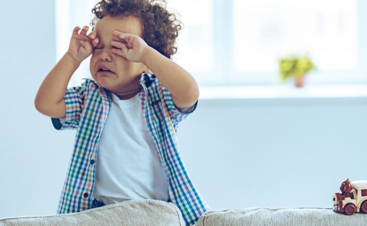 A toddler boy wiping tears from his eyes.