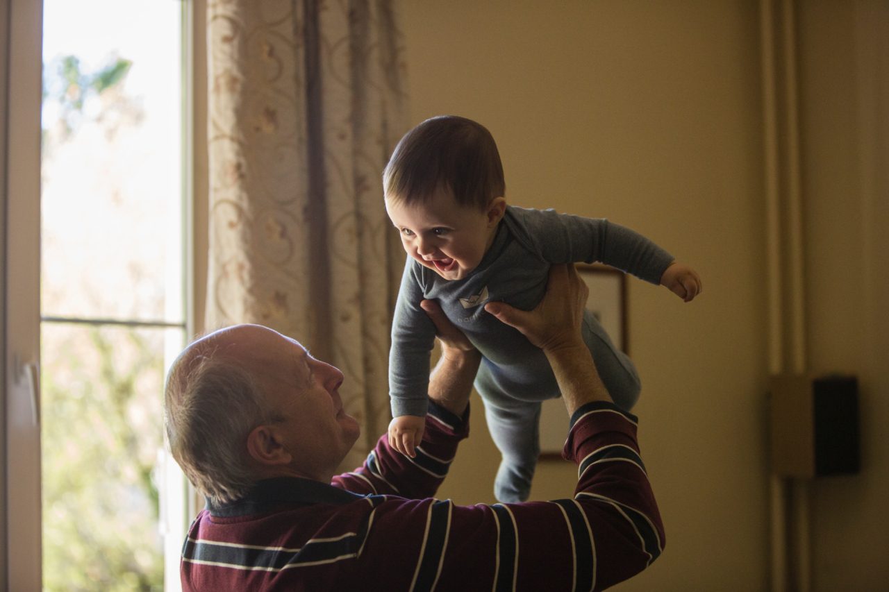 grandpa holds up baby by sunlit window