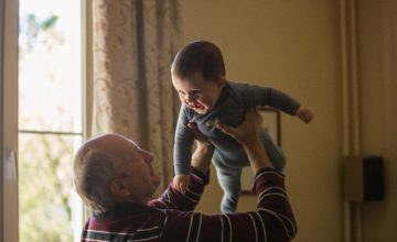 grandpa holds up baby by sunlit window
