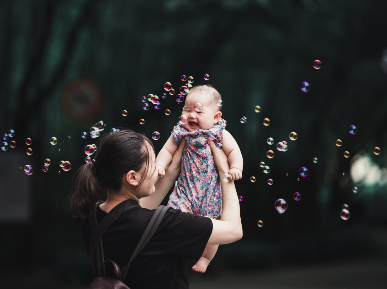 mom holds baby up trees bubbles
