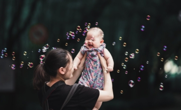 mom holds baby up trees bubbles