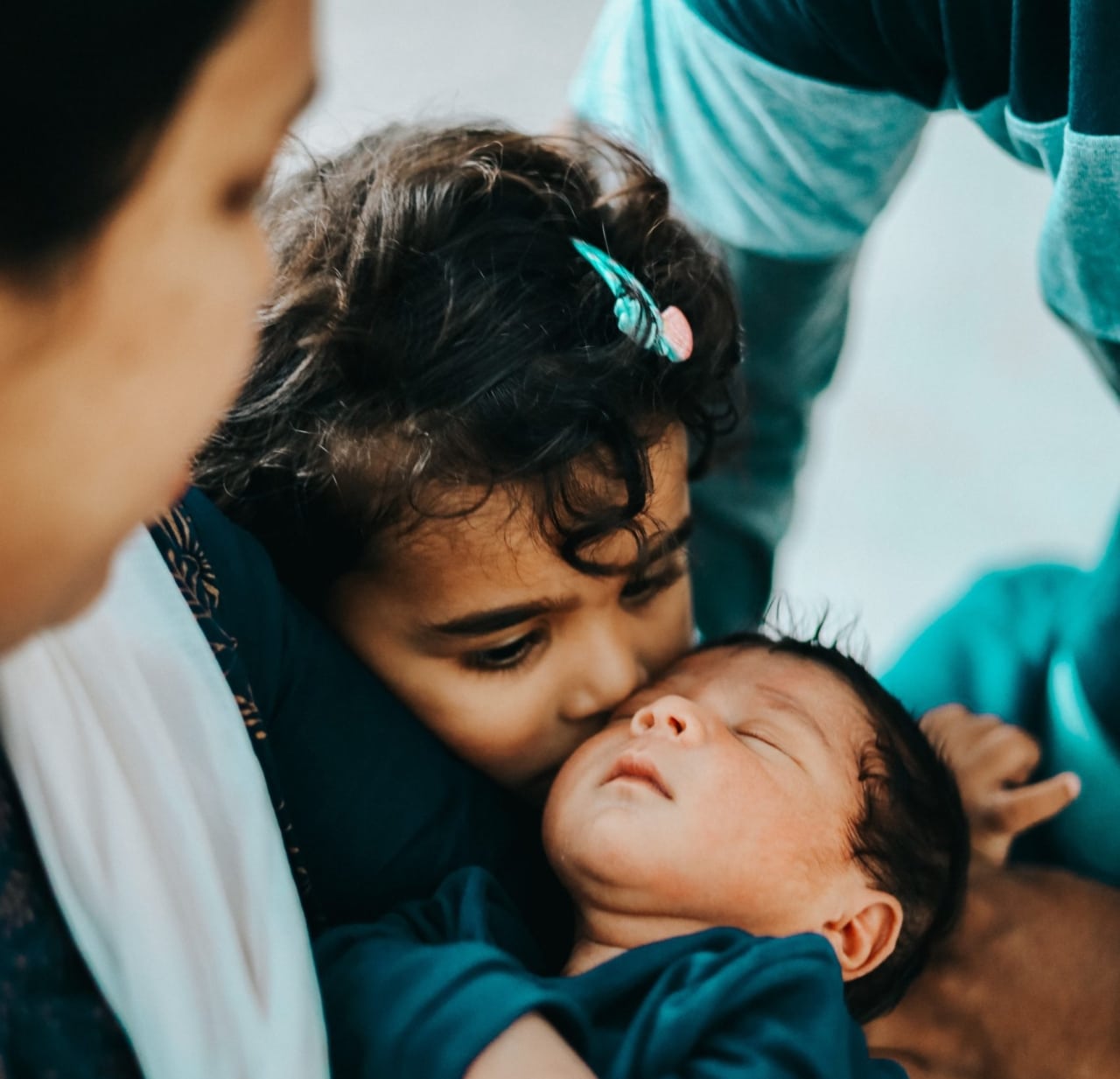 sister kisses baby in mom's arms