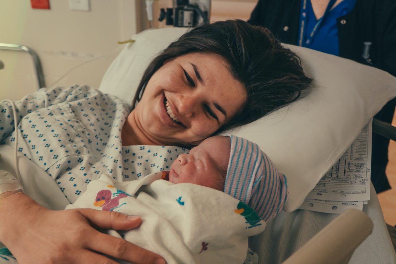 Mother smiles at newborn in hospital bed