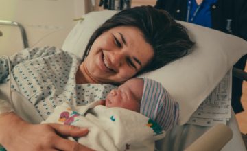 Mother smiles at newborn in hospital bed