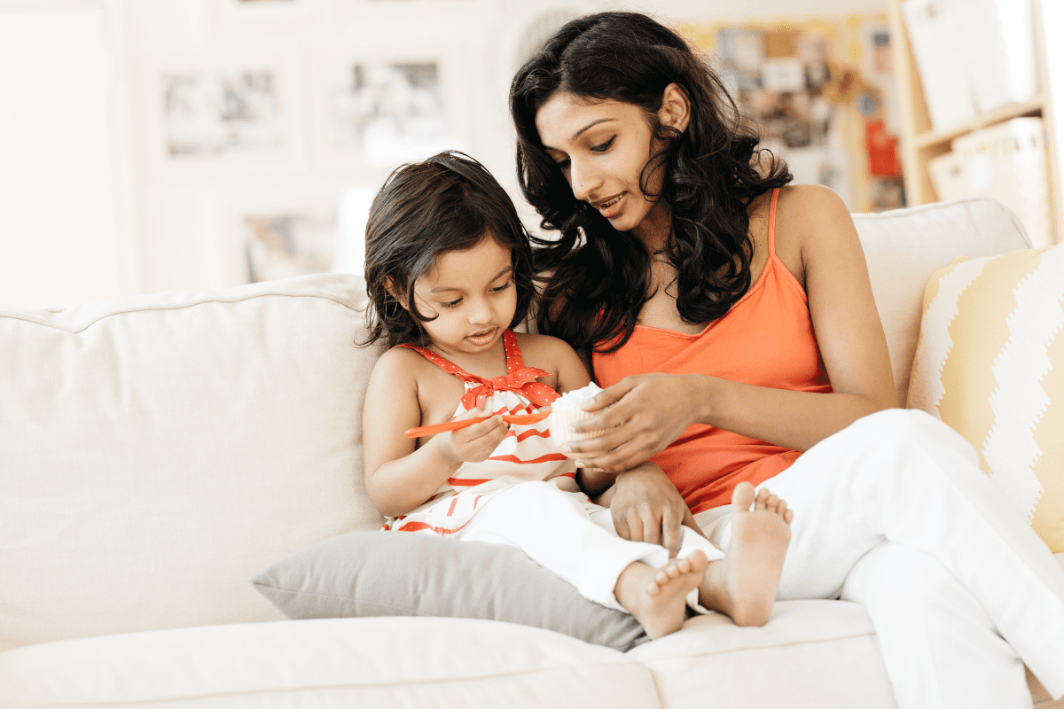 Mother and daughter wearing orange sit on couch