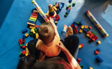 Child sitting in adults lap and playing with Lego toys