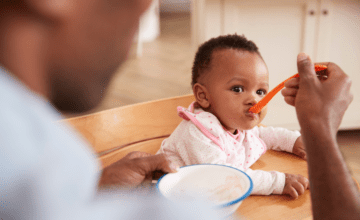 Father feeds baby with red spoon