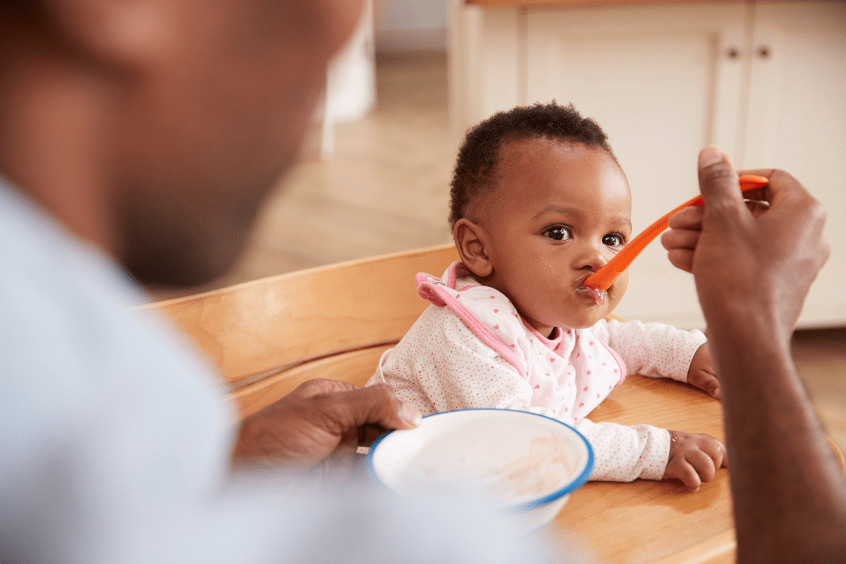 Father feeds baby with red spoon