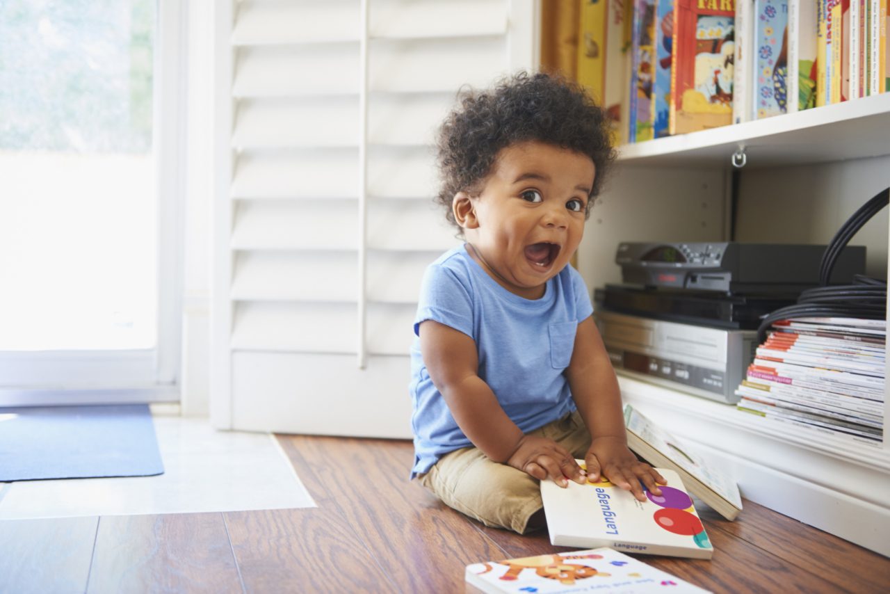 Surprised Black baby boy sitting on floor playing with books