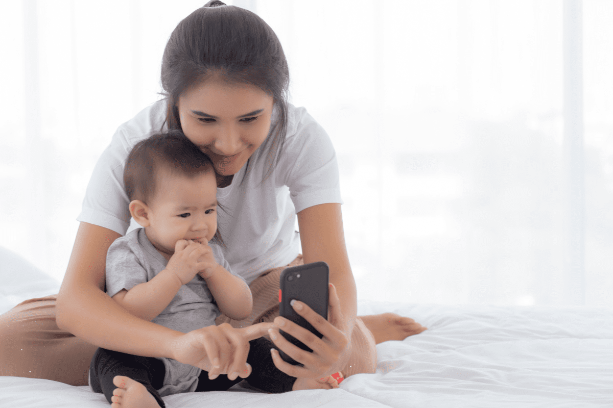 mom sits on bed and shows phone to child