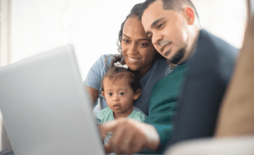 parents look at laptop with baby wearing bow