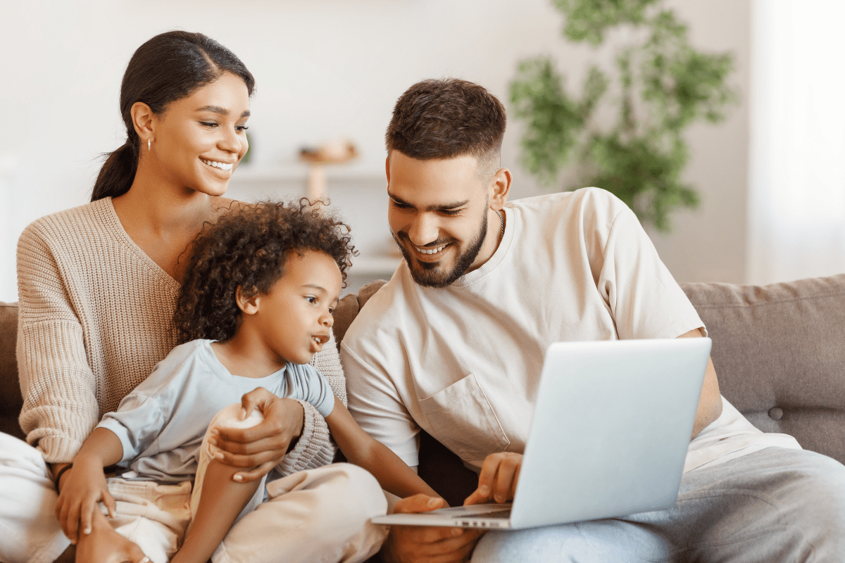 parents and baby look at laptop sitting on couch