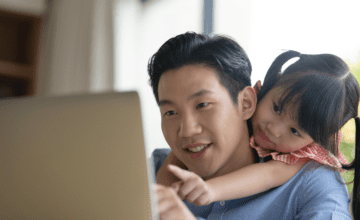 daughter hugs dad from behind while watching laptop