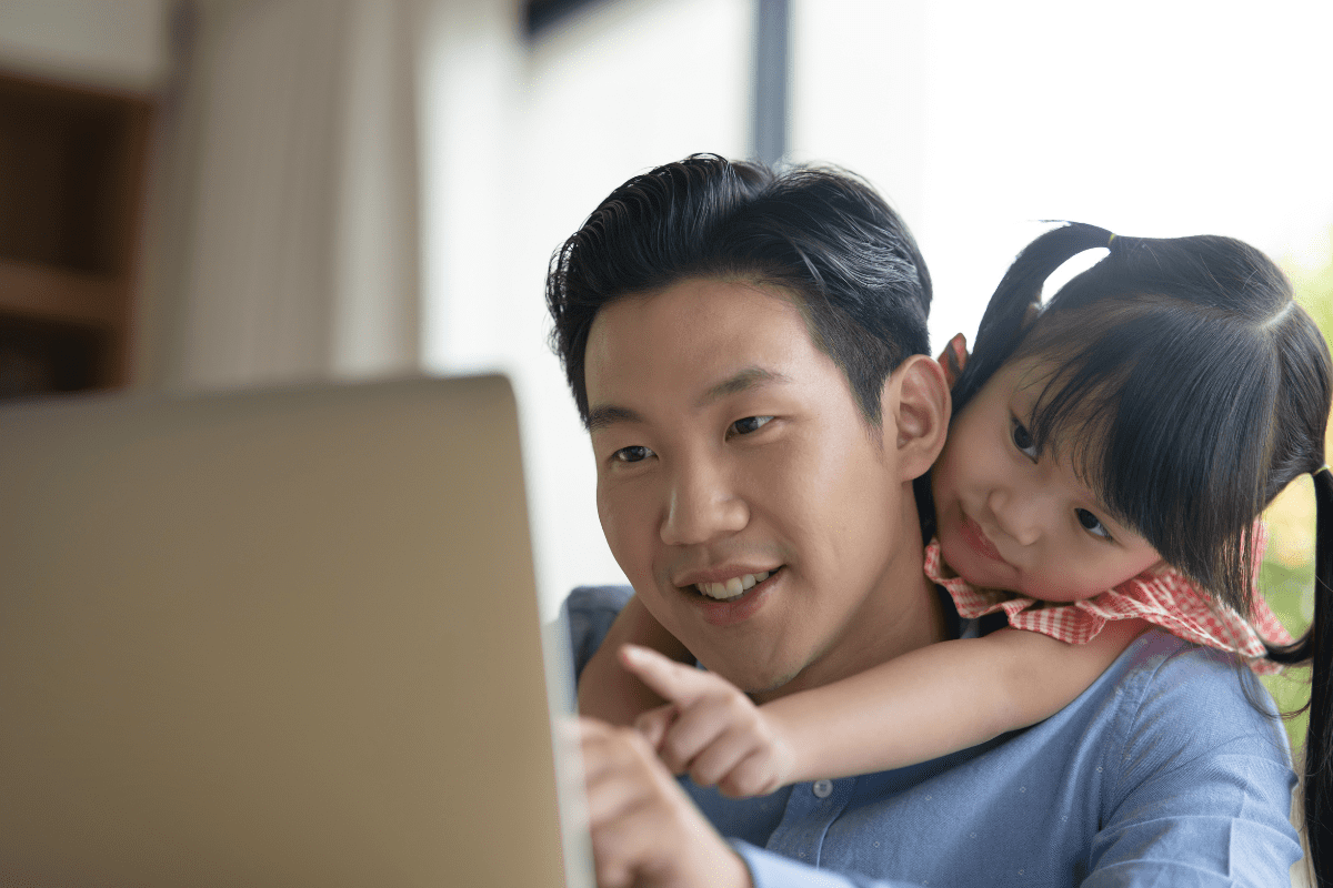daughter hugs dad from behind while watching laptop