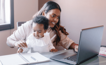 mom holds child and works on laptop
