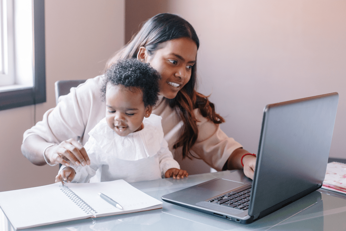 mom holds child and works on laptop