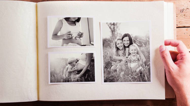 Black and white pictures in a photo album, two children and adult woman and a pregnant woman with a cjild kissing her stomach and a pregnant woman's mid torso