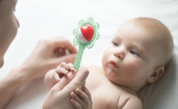Adult holding infant toy and infant holding the hand holding the toy