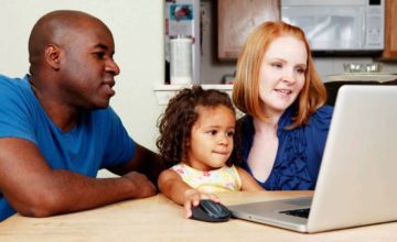 Two aduclts with child looking at open laptop