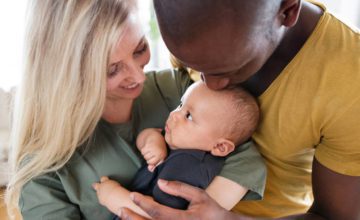 Man and woman holding infant, man kissing infant on head