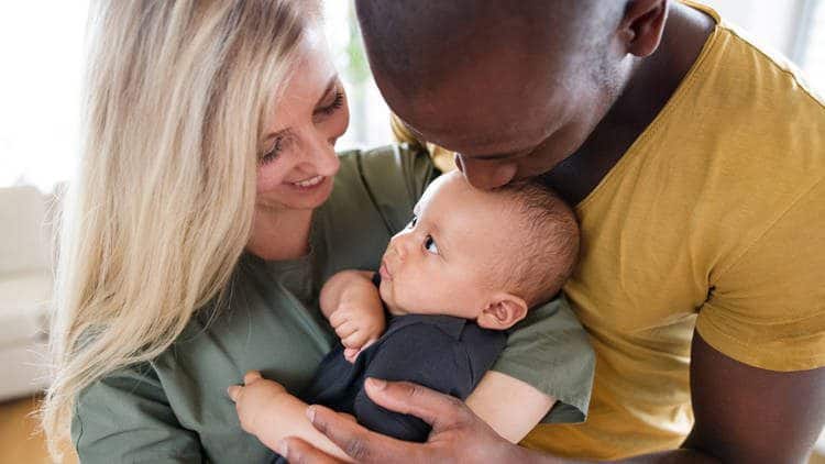 Man and woman holding infant, man kissing infant on head