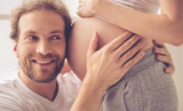 Smiling man with ear to pregnant belly