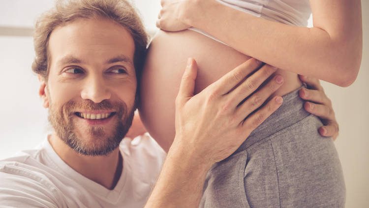 Smiling man with ear to pregnant belly