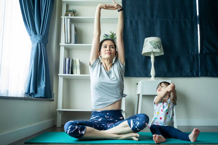 Woman stretching on a mat with a toddler stretching too
