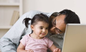 Dad and little girl sit together in front of a screen