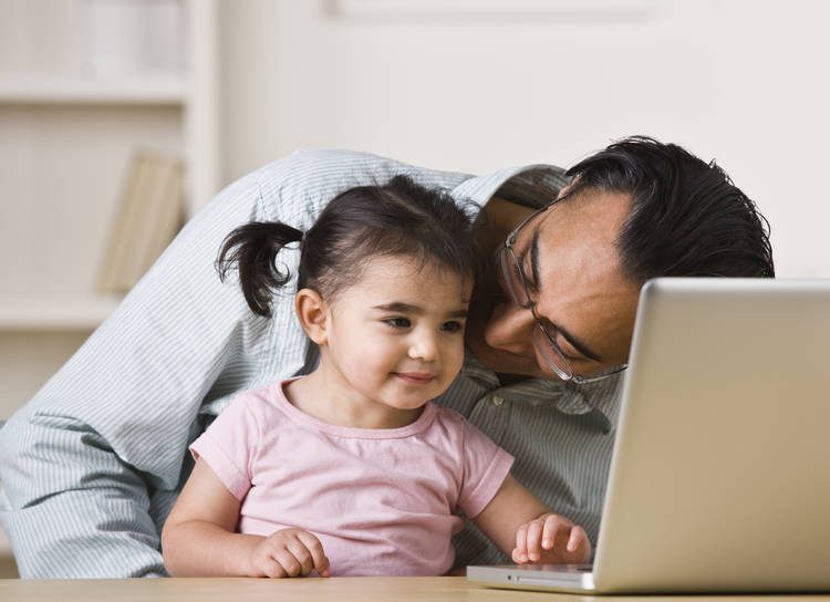 Dad and little girl sit together in front of a screen