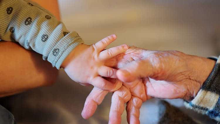 Elderly hand holding an infants hand.