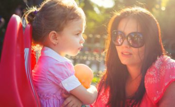 Child with arms crossed and woman with sunglasses looking at her