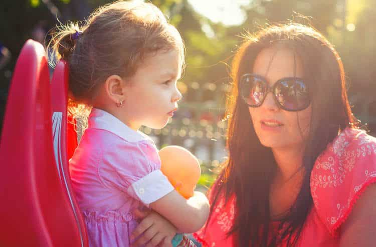 Child with arms crossed and woman with sunglasses looking at her